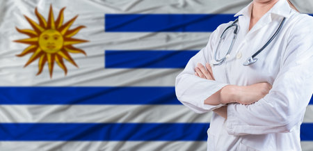 Doctor with crossed arms on Uruguay flag. Uruguay health and care concept. Female doctor on Uruguay flagの写真素材
