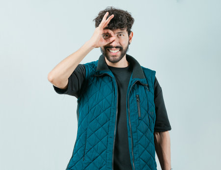 Cheerful guy making ok gesture looking through fingers. Handsome young man making OK gesture looking through fingers isolatedの写真素材