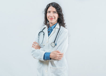 Portrait of smiling latin female doctor with crossed arms on isolated background. Successful young female doctor with crossed arms looking at cameraの写真素材