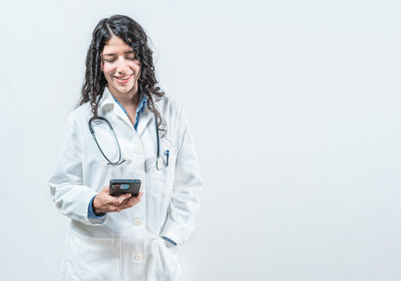 Smiling female doctor using smart phone isolated. Doctor holding phone, Concept of online medical servicesの写真素材