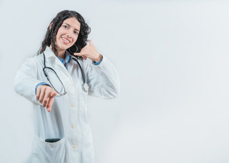 Beautiful female doctor gesturing call isolated. Woman doctor making call gesture and pointing at the cameraの写真素材