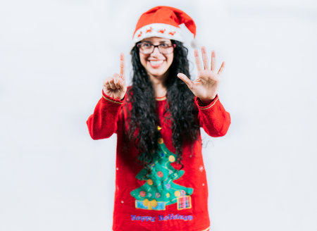 Happy girl in Christmas hat counting number SIX, isolated. Smiling girl in Christmas sweater counting number 6の写真素材