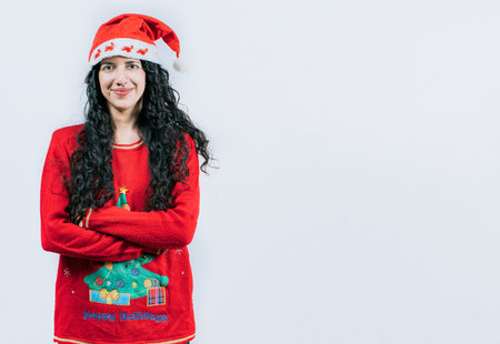 Portrait of smiling Latin girl in Christmas sweater with crossed arms, isolated. Smiling girl in Christmas hat with crossed armsの写真素材