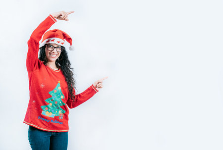 Smiling girl in Christmas sweater pointing to the side, isolated. Happy young woman in Christmas sweater pointing asideの写真素材