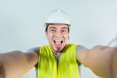 Funny builder engineer taking a selfie isolated, Engineer taking a selfie isolated. View of male engineer taking a selfie. Smiling male engineer taking a selfie looking at cameraの写真素材