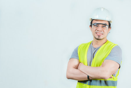 Portrait of smiling engineer with arms crossed isolated. Young engineer with helmet and vest...