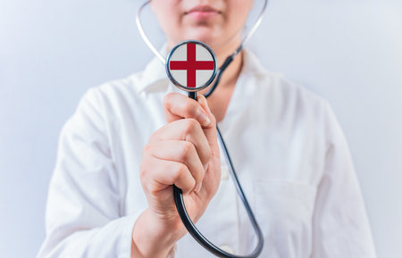 Female doctor holding stethoscope with England flag. National health system of Englandの写真素材