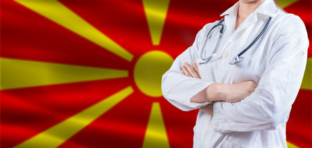 Doctor with crossed arms on North Macedonia flag. North Macedonia health and care concept. Female doctor on North Macedonia flagの写真素材