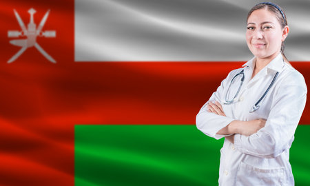 Female doctor on Oman flag. Doctor with crossed arms on Oman flag. Oman health and care conceptの写真素材