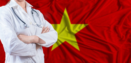 Doctor with crossed arms on Vietnam flag. Vietnam health and care concept. Female doctor on Vietnam flagの写真素材