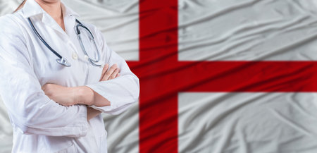 Doctor with crossed arms on England flag. England health and care concept. Female doctor on England flagの写真素材
