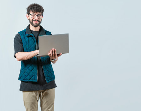 Smiling Bearded guy using laptop and looking at camera isolated. Handsome young man with glasses laptop and looking at cameraの写真素材