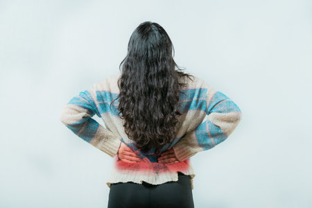 Suffering young woman with pain holding her back isolated. Female with spine problems isolated. Lumbar problems. woman with pain holding her backの写真素材
