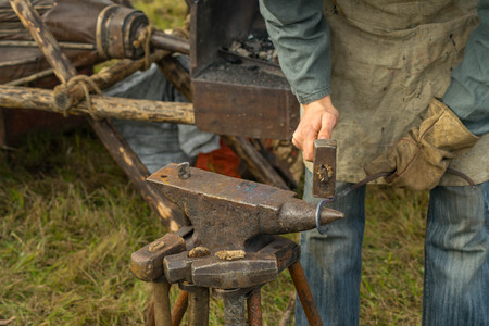 Blacksmith working with metal at the anvil at the summer