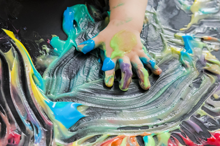 baby painting with colored paint with his handsの写真素材