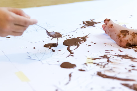 baby sitting painting with hands with chocolateの写真素材