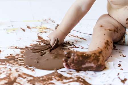 baby sitting painting with hands with chocolateの写真素材