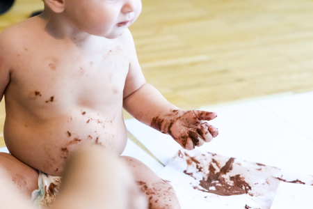 baby sitting painting with hands with chocolateの写真素材