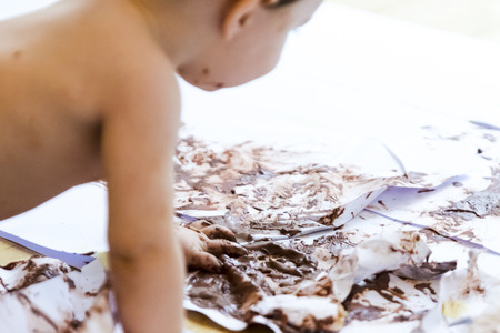 baby sitting painting with hands with chocolateの写真素材