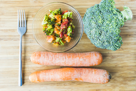 broccoli salad with carrot in glass bowl on wooden boardの写真素材