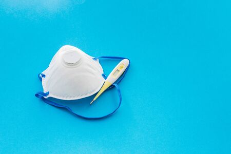 A thermometer and mask for coronavirus protection with copyspace on blue background