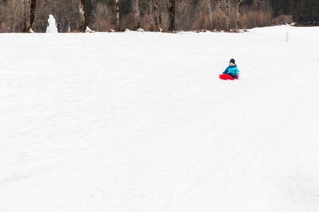 A boy with red sled in the snowの写真素材