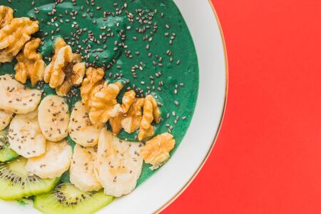 A spirulina smoothie bowl with banana, walnuts, kiwi and chia seeds on red backgroundの写真素材