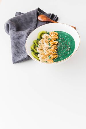 A spirulina smoothie bowl with banana, walnuts, kiwi and chia seeds on white backgroundの写真素材