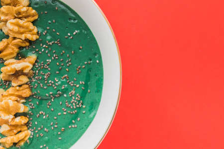A spirulina smoothie bowl with banana, walnuts, kiwi and chia seeds on red background