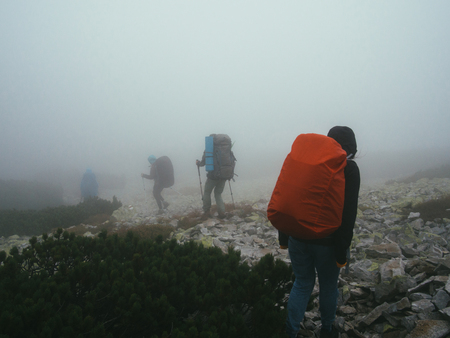 Tourists travelers with backpacks walking through the rocks in thick mist of milk. Poor visibility...