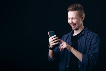 Cheerful Youngster in Jeans Shirt and T-shirt Using Smartphoneの写真素材