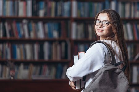 Cheerful student standing in university library with books