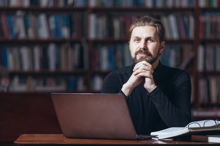 Mature man working at library with laptop and booksの写真素材