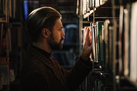 Side view of bearded man choosing book at public library
