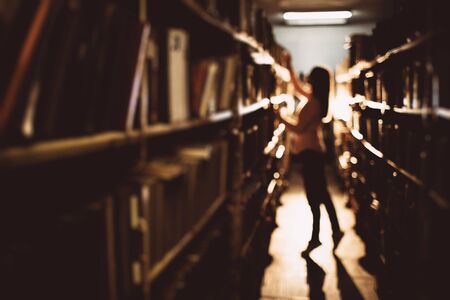 Blur background of young lady choosing book at library