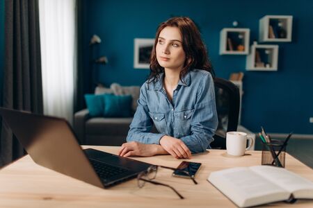 Young girl sitting at table with laptop and looking away