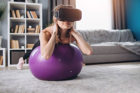 Young girl in virtual glasses doing abs on fitness ball