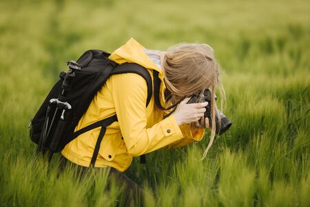 Professional photographer in yellow jacket standing among wheat field and taking pictures of ears....
