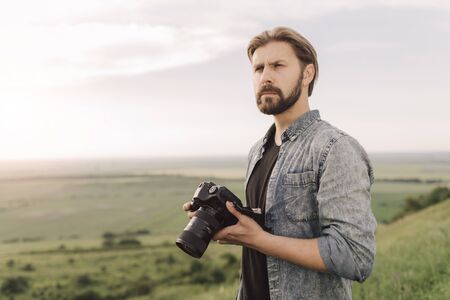 Handsome man standing on high hill with digital cameraの写真素材