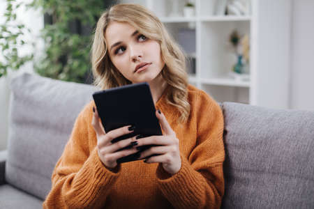 Dreamy woman sitting on sofa with tablet