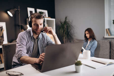 Man having video chat on laptop while woman reading book