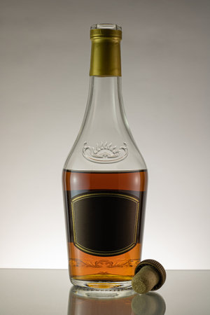 Still life brandy bottle and cork of cognac on gray background. VIP class alcoholic drink. Brown...