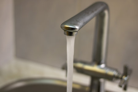 Mixer tap with flowing water. The faucet is open in the kitchen and water is flowing.の写真素材