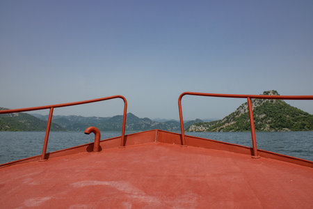 Red boat in the Skadar lake on the foreground. Bow of the ship close-up. Mountains and blue sky on the background.の写真素材
