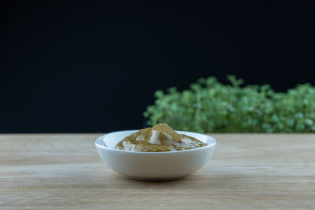 Condiment mustard in white plate on wooden platform. Nutrition spicy seasoning organic food. Micro greens plant spice salvia hispanica grow on black background. Germination of herbの写真素材