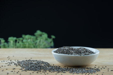 Still life black chia seeds in white plate on wooden platform. Micro greens plant salvia hispanica grow on black background. Germination of herb cereal seeds. Healthy nutrition.の写真素材