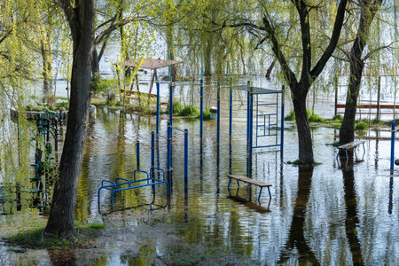 Flood on bank river in spring time. Water filled play and sport grounds in city. Overflowed bank with sunken trees. Bottling shoreline flow and natural disaster. Climate change.の写真素材