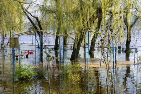 Flood on bank river in spring time. Water filled play and sport grounds in city. Overflowed bank with sunken trees. Bottling shoreline flow and natural disaster. Climate change.の写真素材