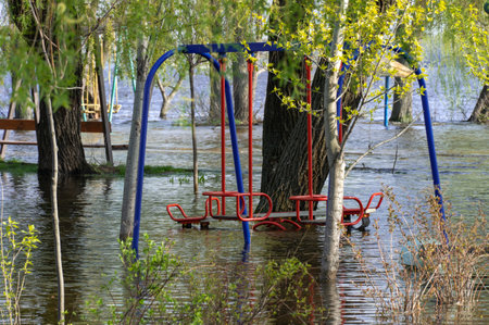 Flood on bank river in spring time. Water filled play and sport grounds in city. Overflowed bank with sunken trees. Bottling shoreline flow and natural disaster. Climate change.の写真素材