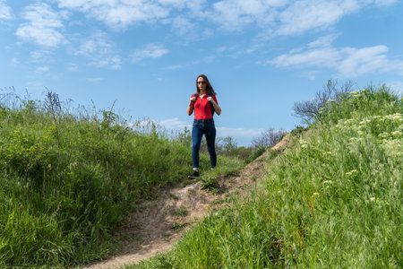 Tourist woman with backpack walking in deciduous forest. Active adult leisure of hiking in green...